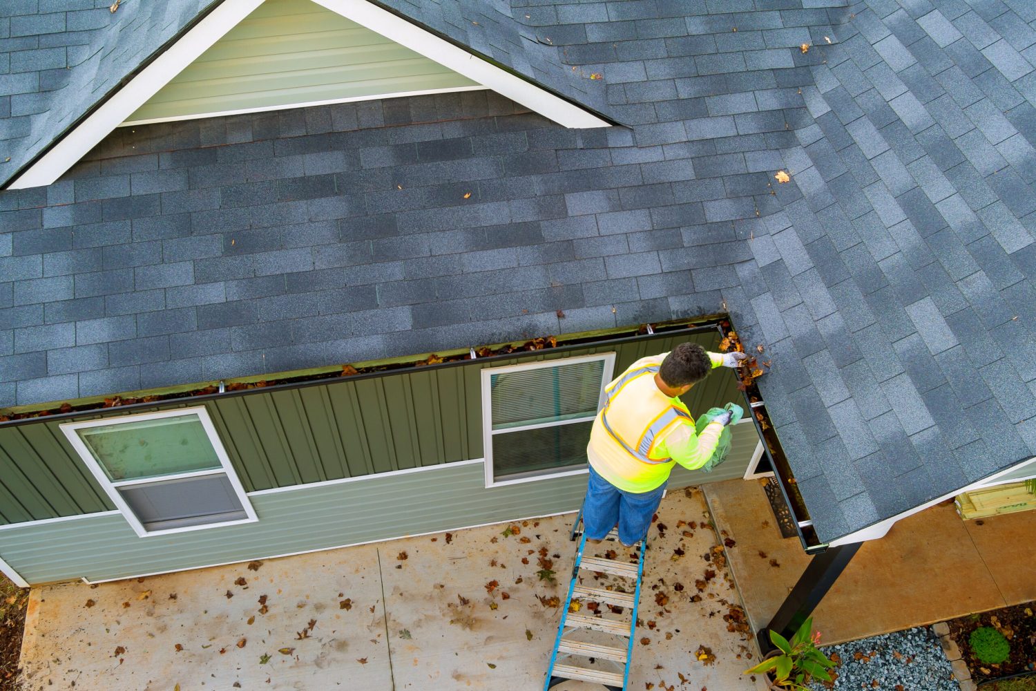 Worker is cleaning clogs in roof gutter drain by picking up dirt, debris, fallen leaves